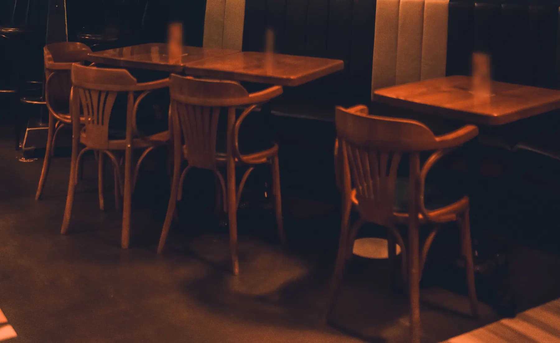Un pub le soir, ses tables en bois et ses chaises vides devant une banquette, dans une lumière chaude.