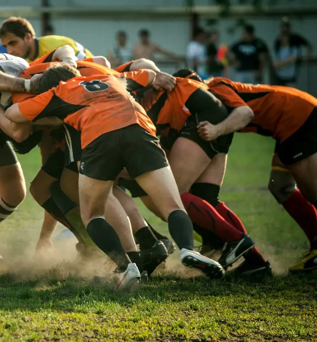 Une mêlée de rugby dans la poussière d’un terrain en herbe.