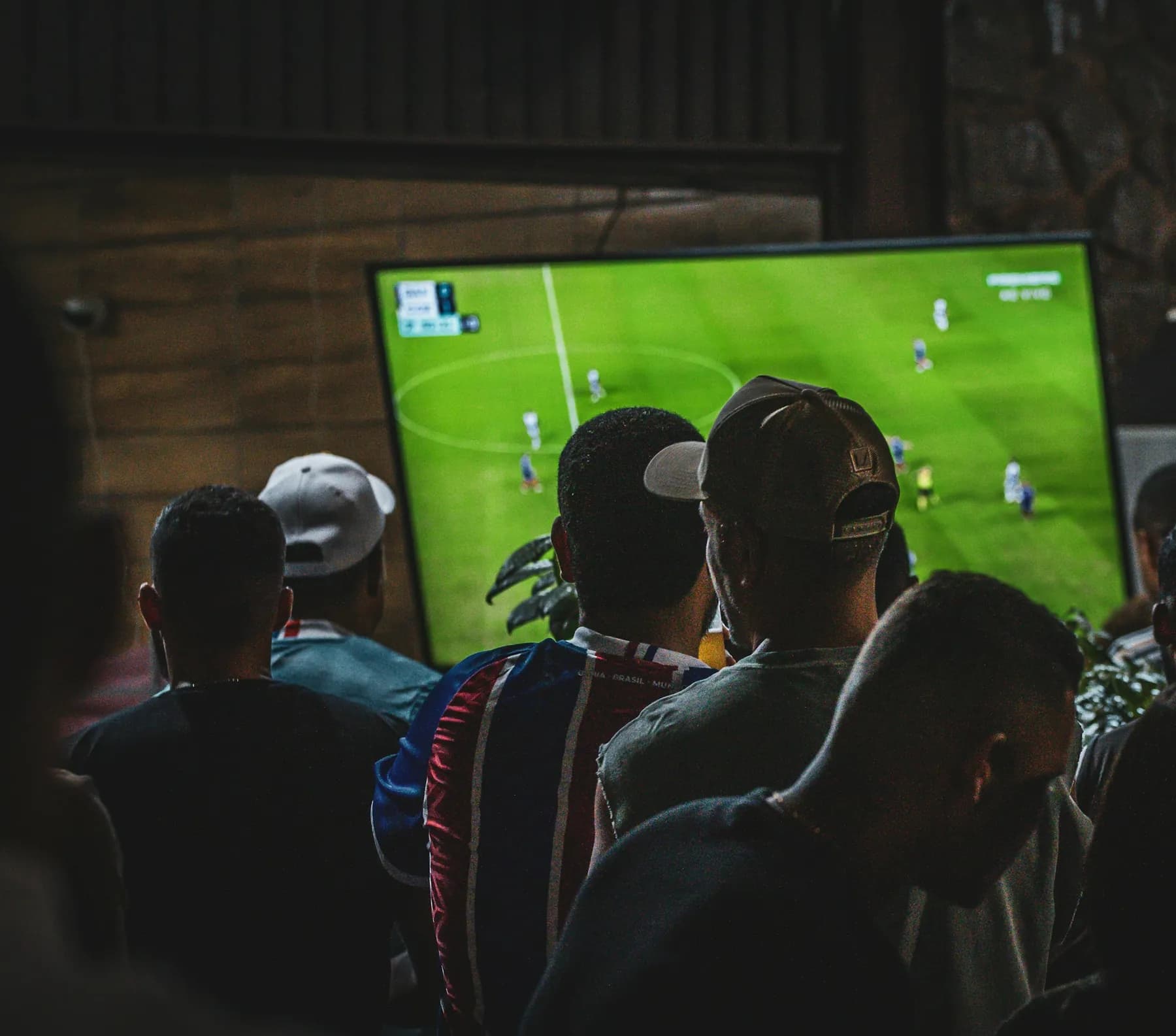 Des clients de dos regardent un match sur un grand écran, dans un bar.