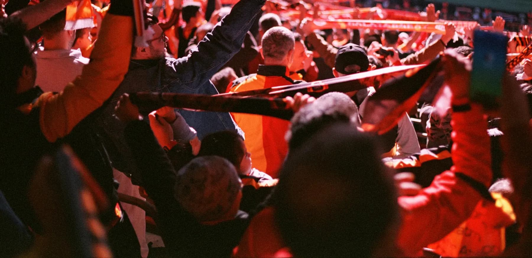 Une tribune de supporters en rouge, les écharpes tendues au-dessus des têtes.