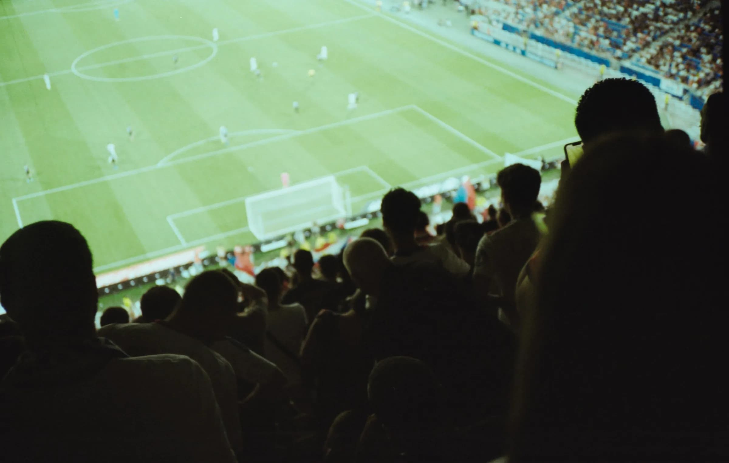 Du haut d’une tribune, des supporters de dos regardent la pelouse éclairée d’un stade.