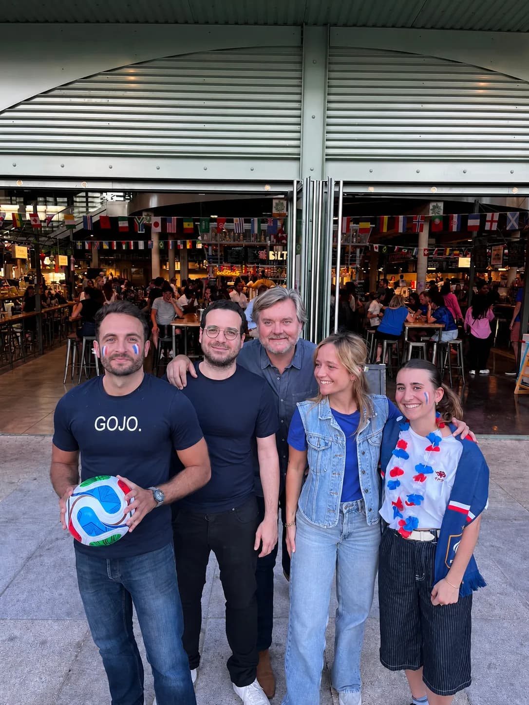 Devant la Halle Biltoki de Rueil-Malmaison grande ouverte, le soir du premier match des Bleus : cinq personnes souriantes, des drapeaux tricolores peints sur les joues, l’une avec un ballon et un t-shirt GOJO. Derrière elles, la Halle pleine, sous les fanions des pays.