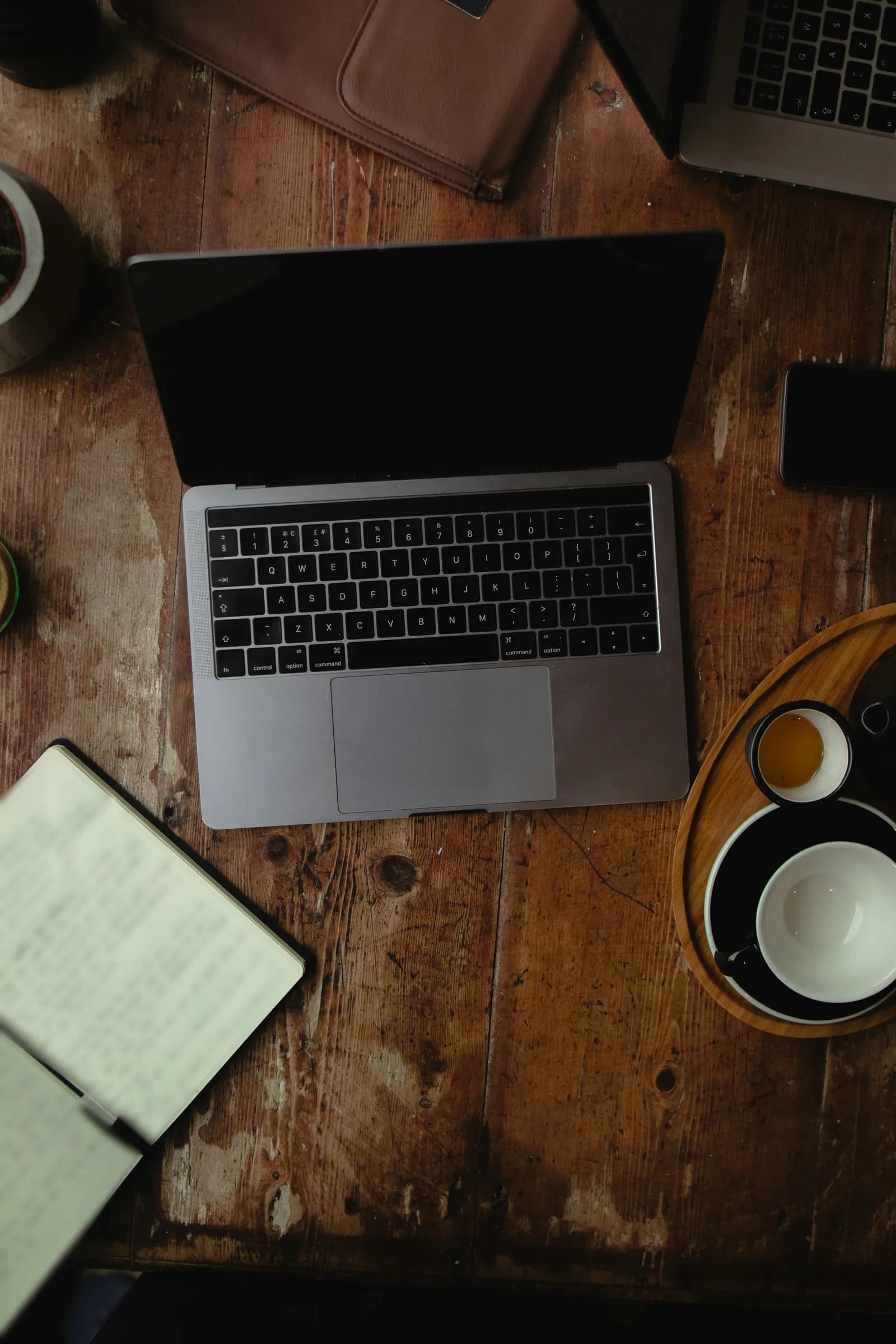 Un ordinateur portable, un carnet ouvert et une tasse sur une vieille table de café en bois, vus de dessus.