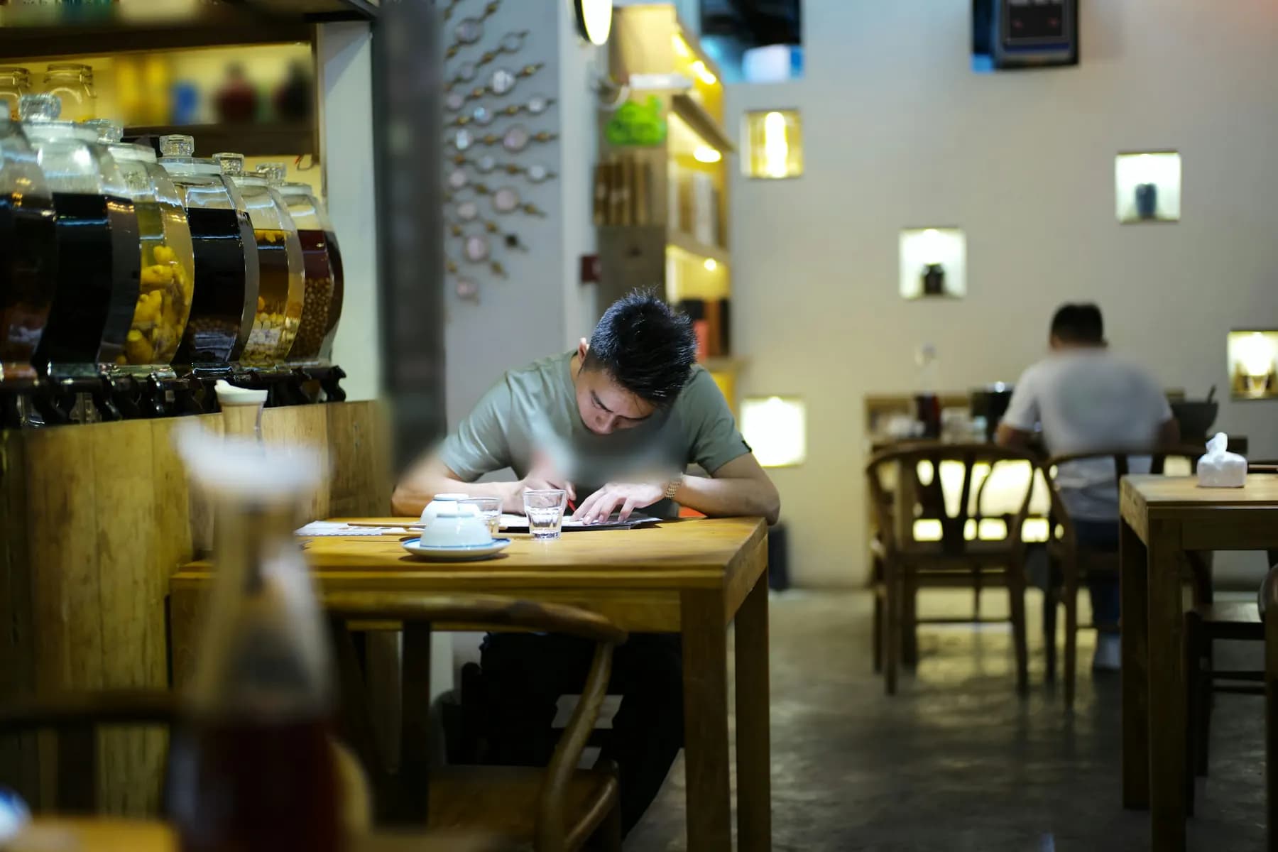 Un homme note au stylo sur des feuilles, attablé dans un restaurant tamisé.