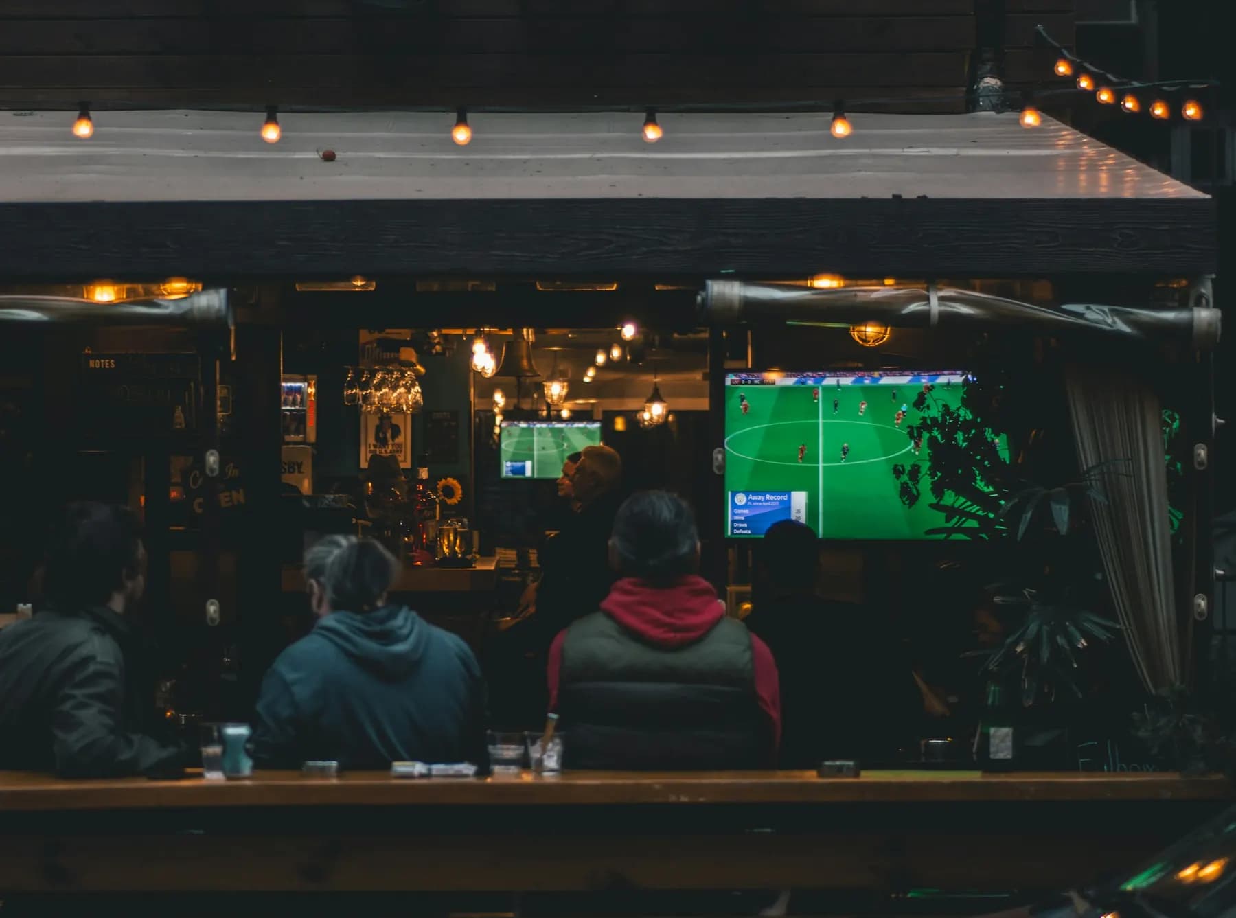 Le soir, des clients installés au comptoir d’un pub regardent un match de football sur les écrans, sous une guirlande d’ampoules.