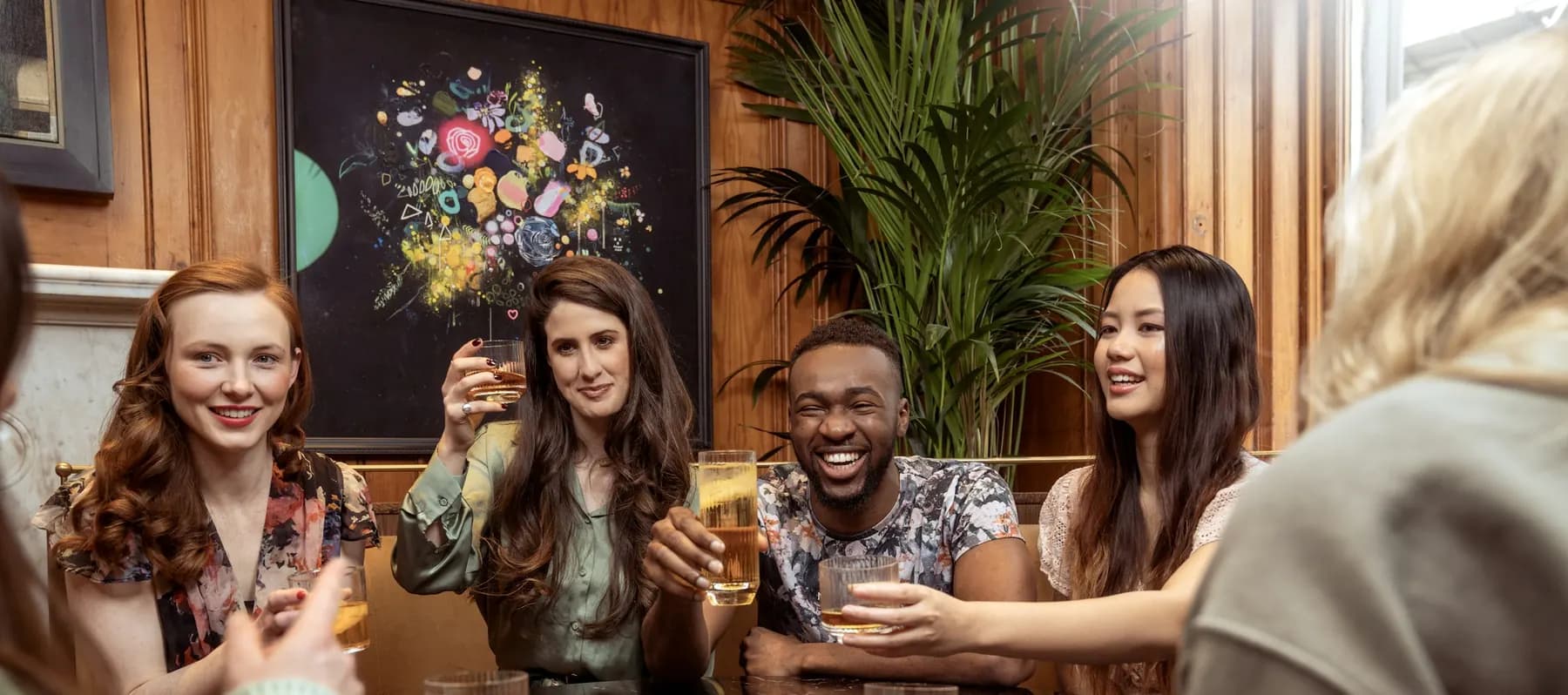 Des amis trinquent autour d’une table, dans un bar aux murs de bois, et rient.