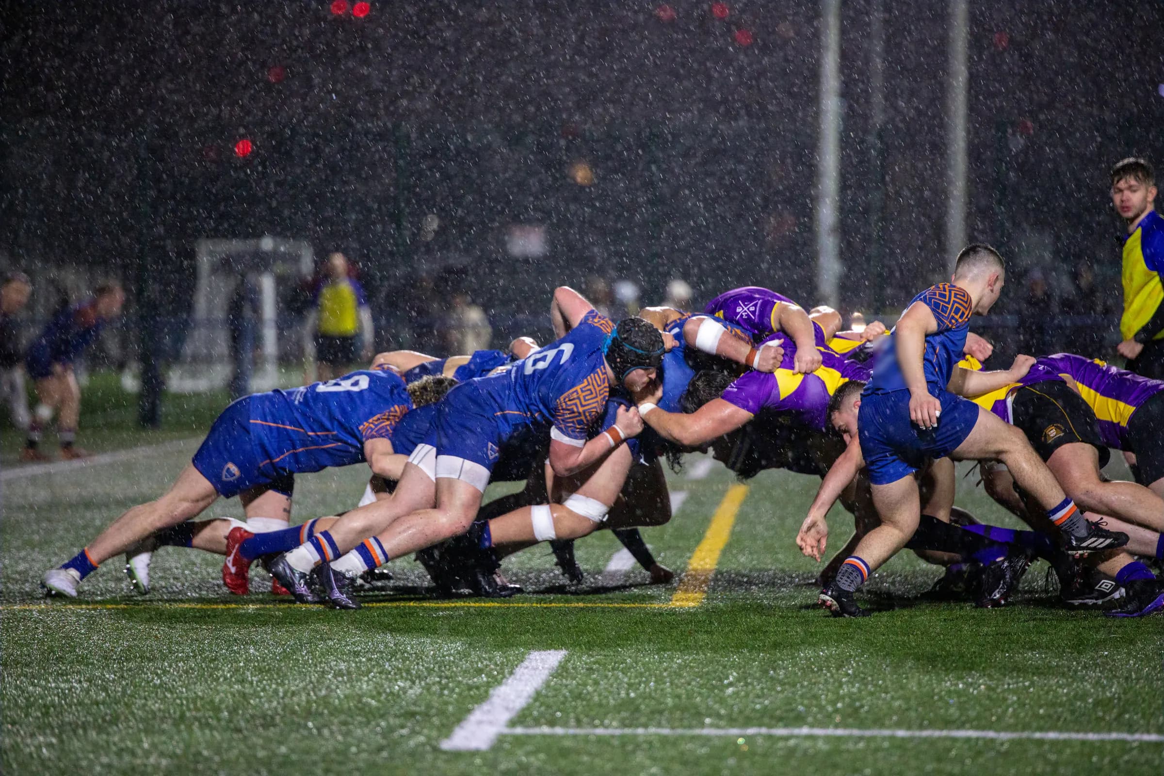 Une mêlée de nuit, sous une pluie battante, les avants poussent sur la pelouse éclairée.