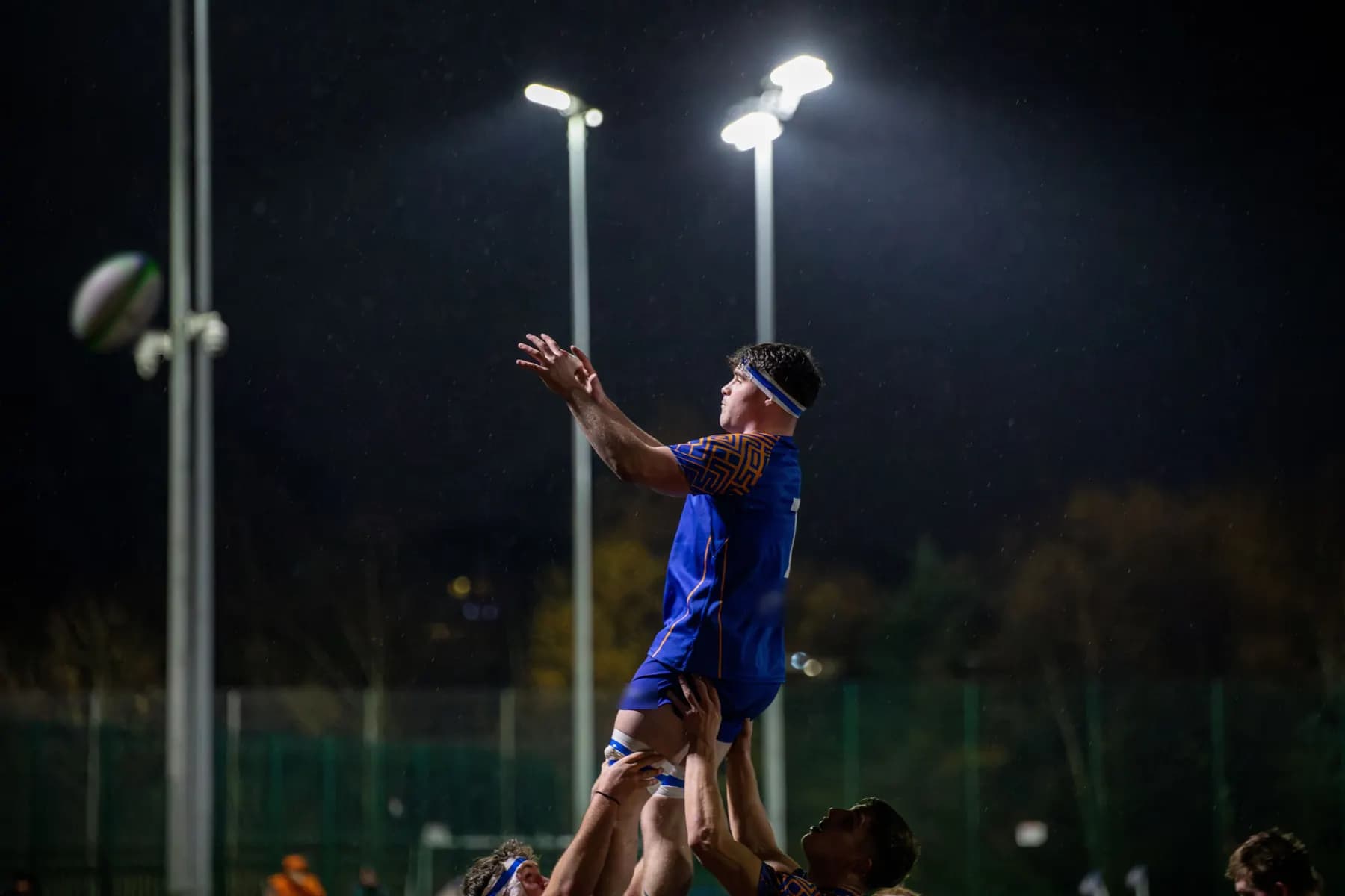 De nuit, sous les projecteurs, un sauteur s’élève en touche vers le ballon.