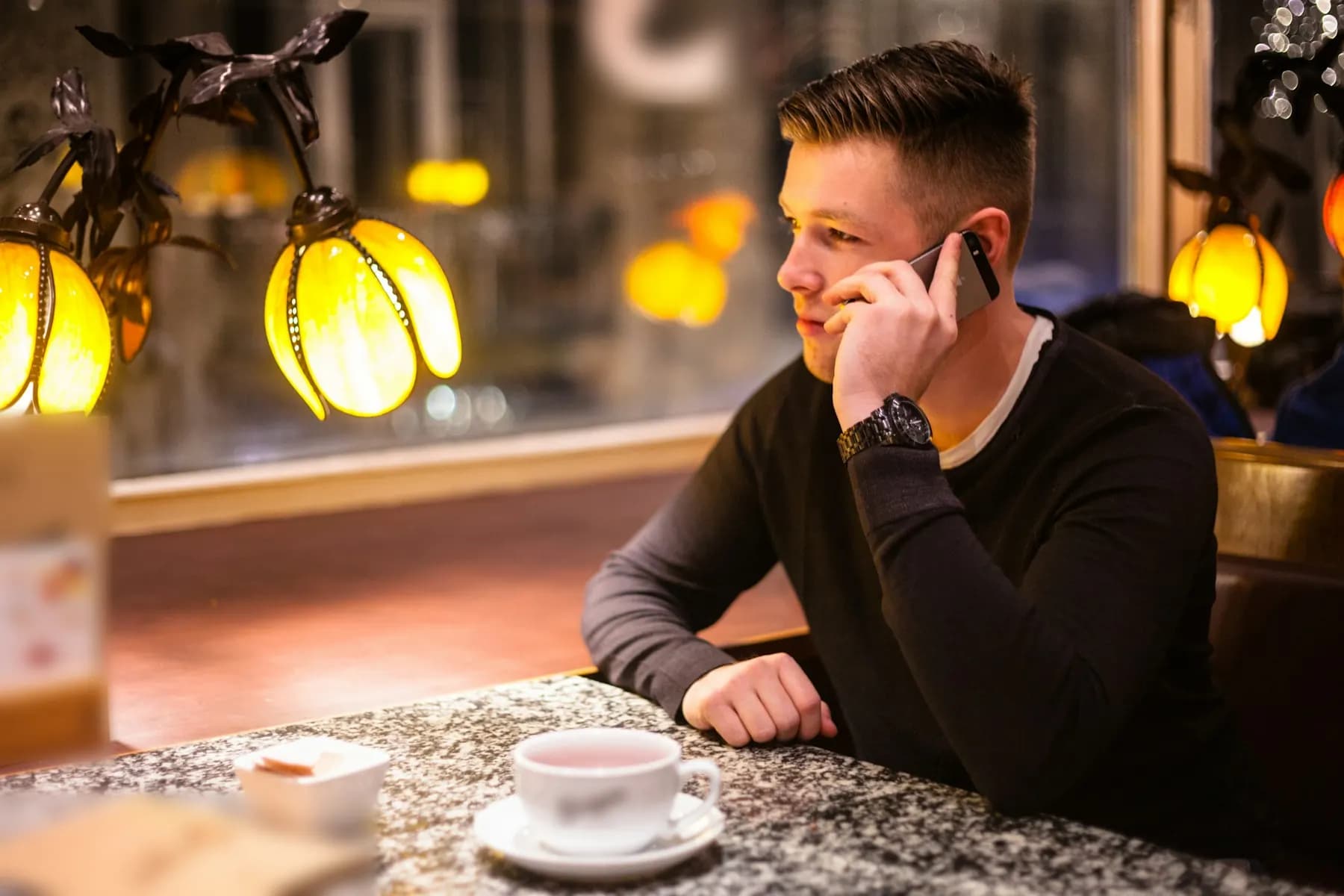 Le soir, dans un café aux lampes en forme de tulipes, un homme en pull sombre téléphone, accoudé à une table de granit, une tasse devant lui.