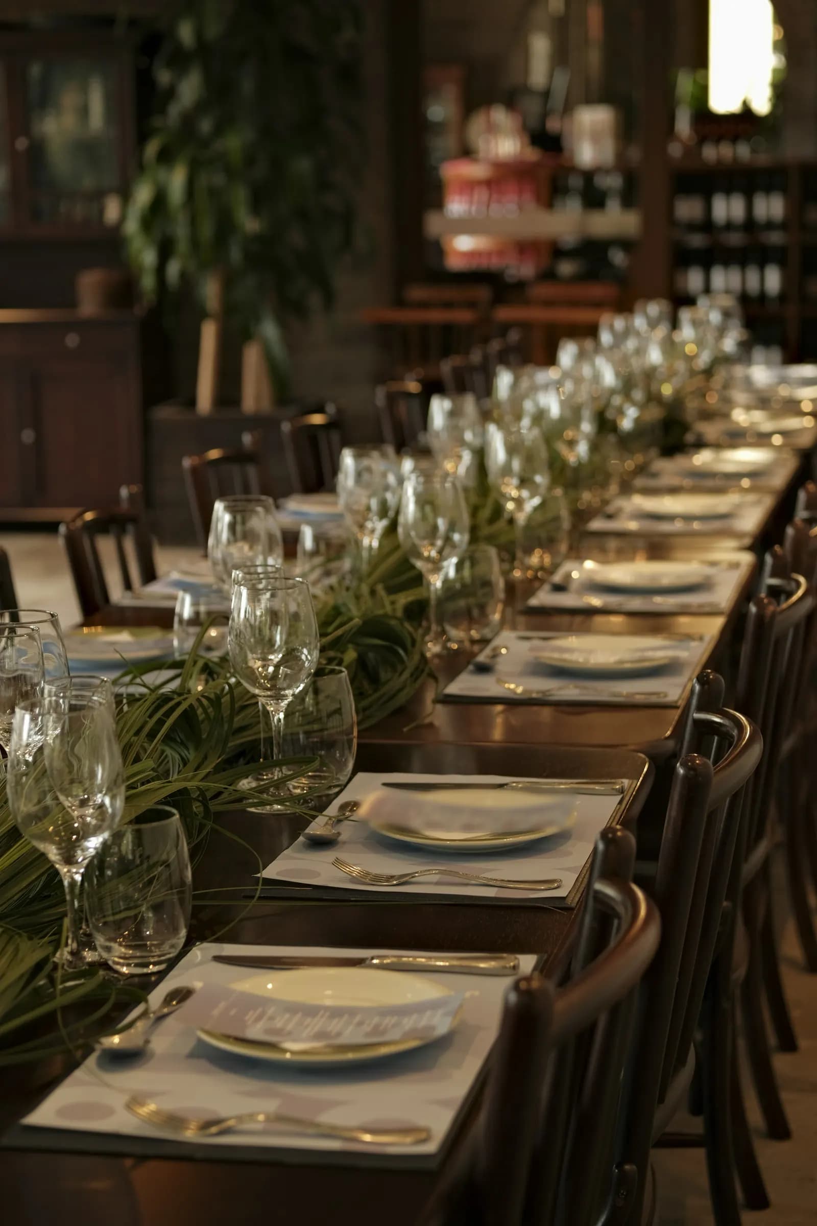Une longue table dressée pour un groupe dans un restaurant, verres alignés et assiettes prêtes.