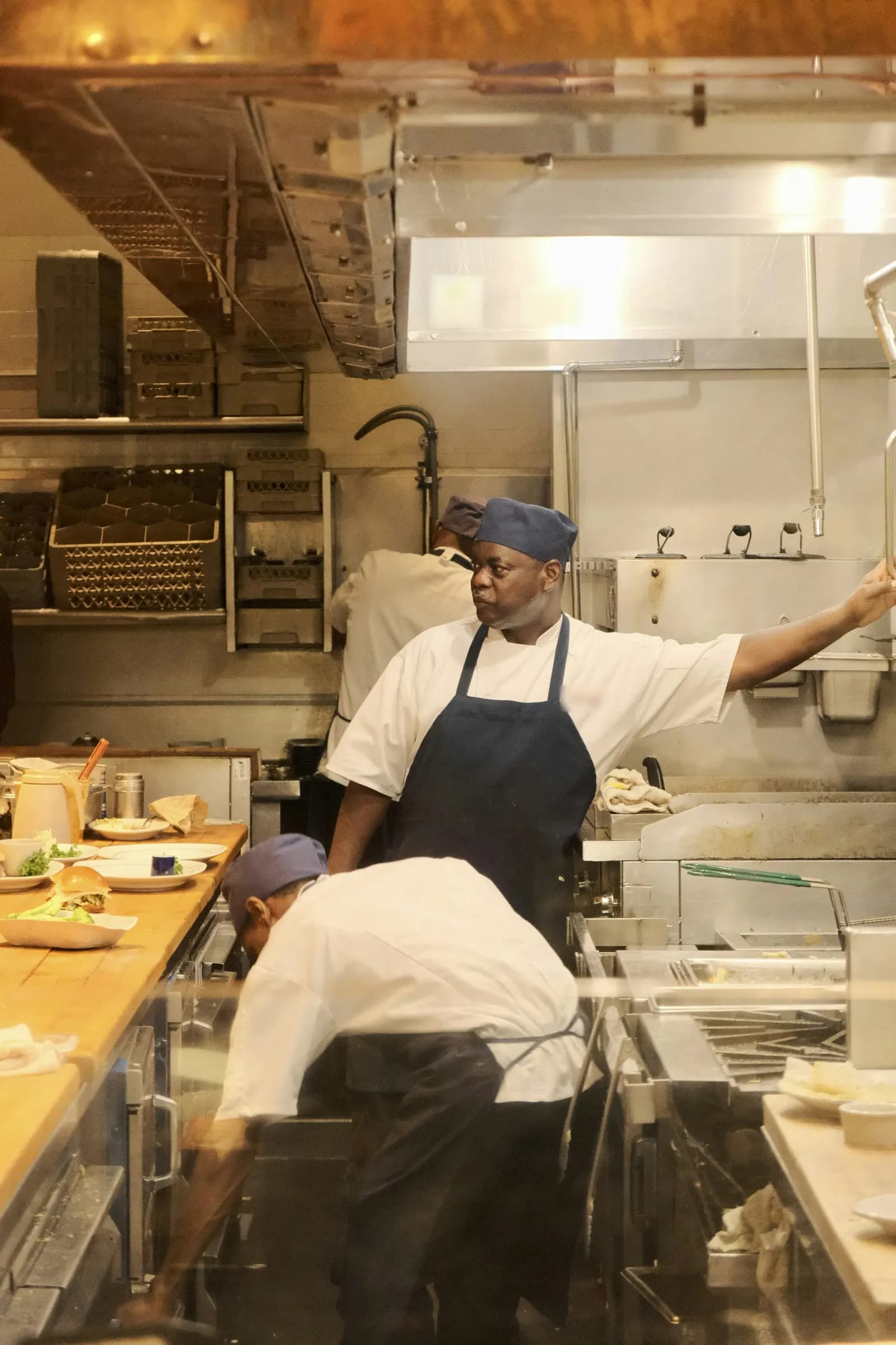 Au passe d’une cuisine de restaurant en plein service, un chef surveille les assiettes prêtes à partir.